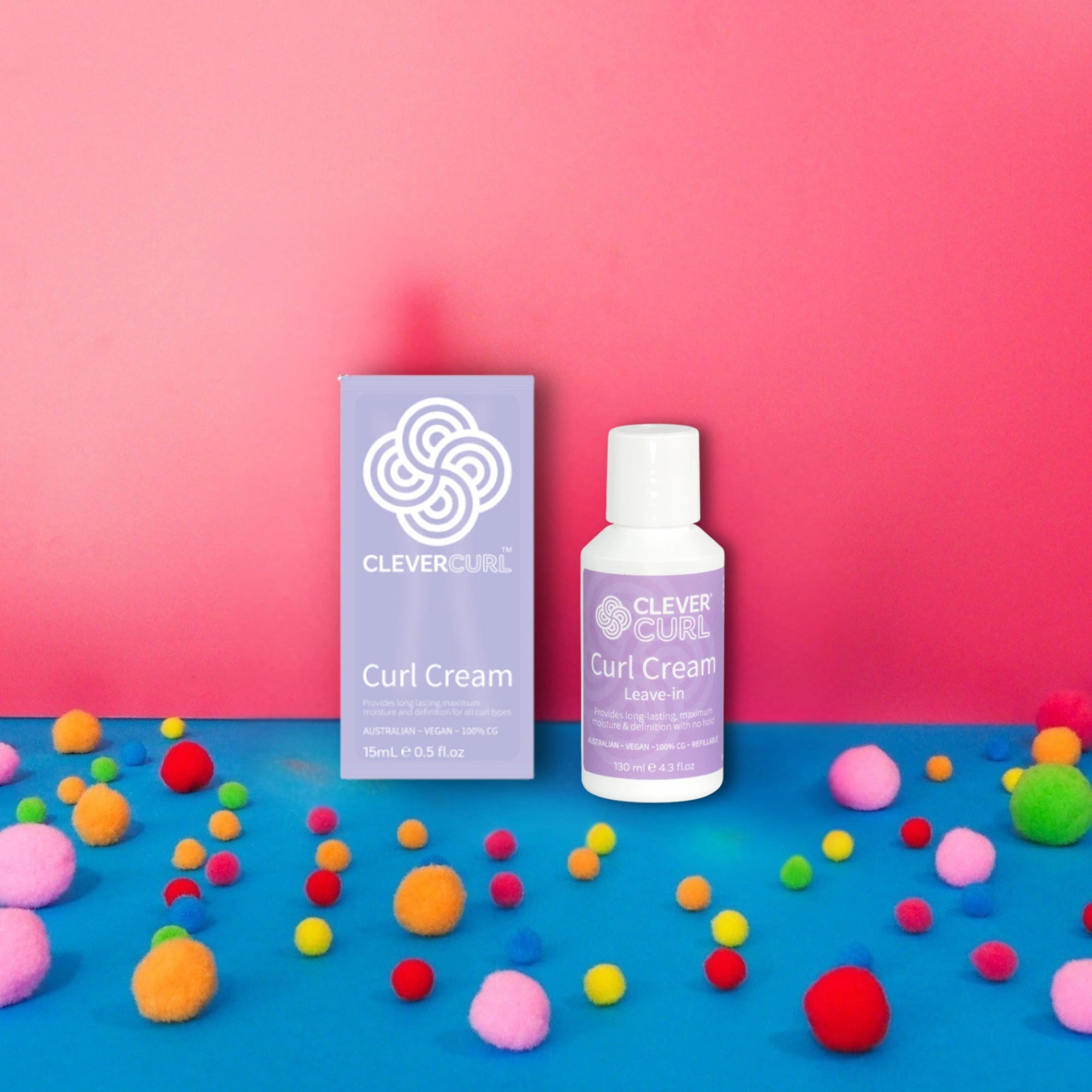 Clever Curl Curl Cream packaging and bottle on a pink and blue background with colorful pom-poms at Curly Tops
